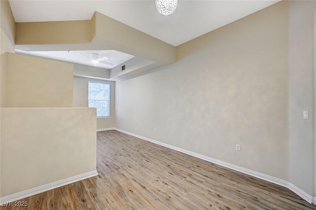 spare room featuring a raised ceiling, wood finished floors, visible vents, and baseboards