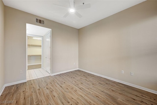 unfurnished room with a ceiling fan, light wood-type flooring, visible vents, and baseboards