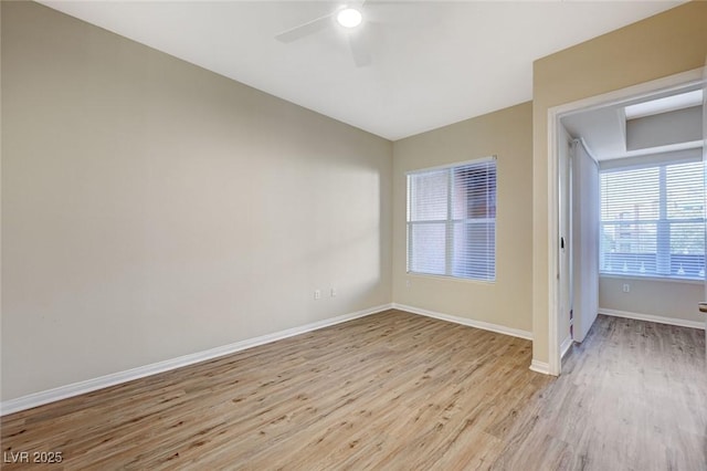 spare room featuring light wood finished floors, a ceiling fan, and baseboards