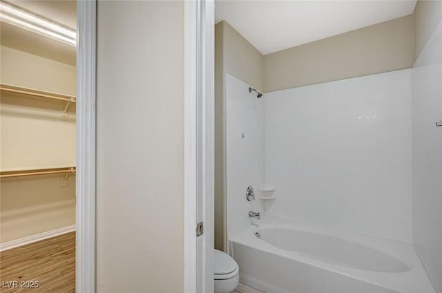 full bathroom with a walk in closet, bathtub / shower combination, toilet, and wood finished floors