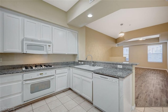 kitchen with white appliances, white cabinetry, a sink, and a peninsula