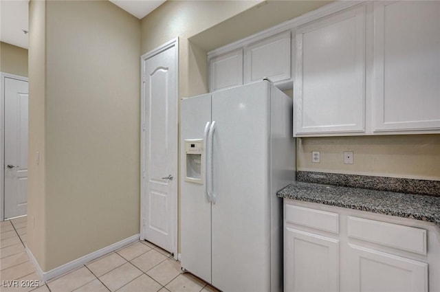 kitchen with light tile patterned floors, white cabinetry, baseboards, white fridge with ice dispenser, and dark stone countertops