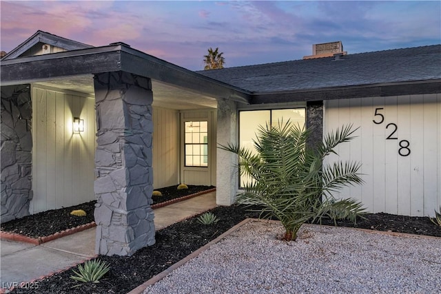 exterior entry at dusk featuring a shingled roof