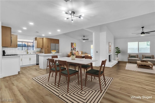 dining space with a brick fireplace, vaulted ceiling, and light wood-style flooring