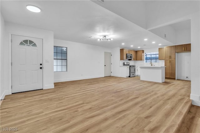 unfurnished living room with recessed lighting, light wood-style floors, baseboards, and a sink