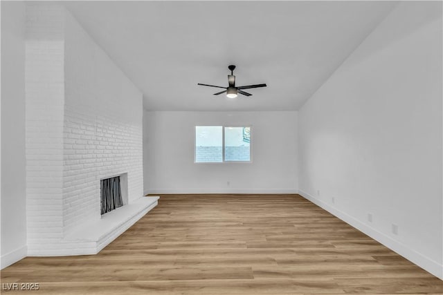 unfurnished living room with ceiling fan, a fireplace, baseboards, and light wood-style floors