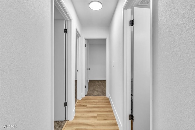 corridor with light wood-type flooring, baseboards, and a textured wall