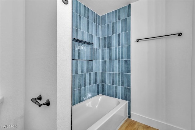 bathroom featuring baseboards, bathtub / shower combination, and wood finished floors