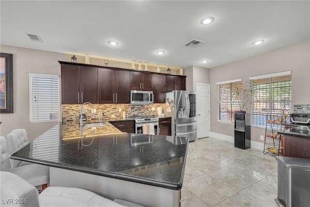 kitchen featuring dark stone countertops, a peninsula, a sink, stainless steel appliances, and tasteful backsplash