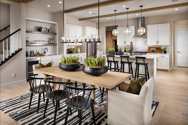 dining space with light wood finished floors, stairway, wet bar, beam ceiling, and recessed lighting