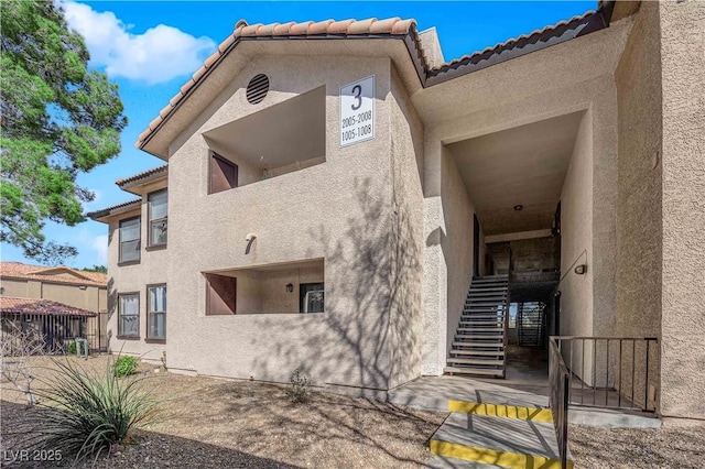 view of property exterior with a tiled roof, fence, stairway, and stucco siding