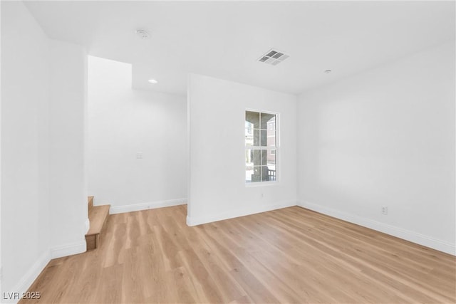 unfurnished room with light wood-style floors, visible vents, stairway, and baseboards