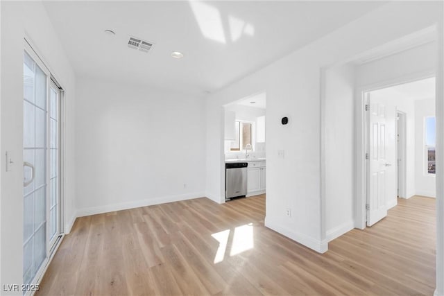 unfurnished living room with light wood-style floors, visible vents, baseboards, and a sink