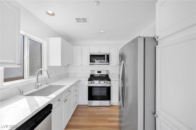 kitchen with a sink, white cabinetry, light wood-style floors, appliances with stainless steel finishes, and light stone countertops