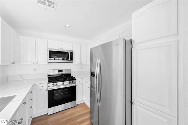 kitchen with visible vents, light stone counters, stainless steel appliances, light wood-style floors, and white cabinetry