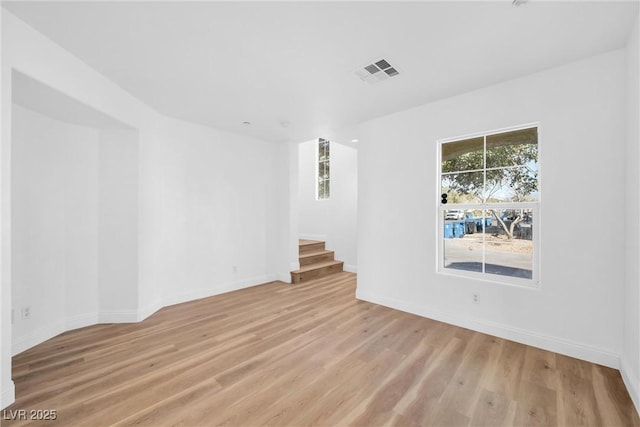 empty room featuring light wood-style flooring, stairway, visible vents, and baseboards