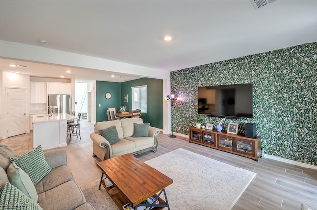 living room with recessed lighting, light wood-style flooring, an accent wall, baseboards, and wallpapered walls