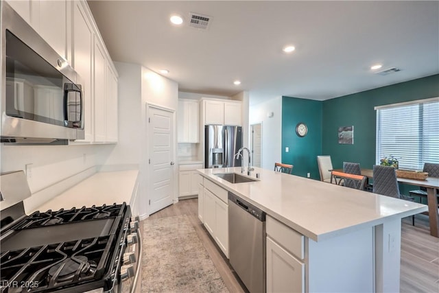 kitchen with a kitchen island with sink, stainless steel appliances, a sink, and light countertops