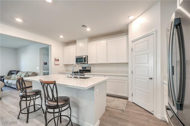 kitchen featuring white cabinets, an island with sink, stainless steel appliances, light countertops, and a sink