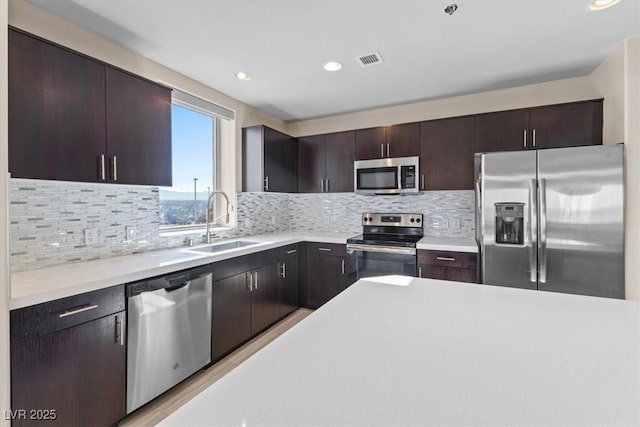 kitchen with a sink, stainless steel appliances, dark brown cabinets, and light countertops