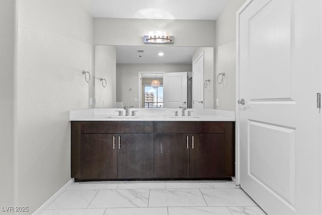 full bath featuring double vanity, marble finish floor, baseboards, and a sink