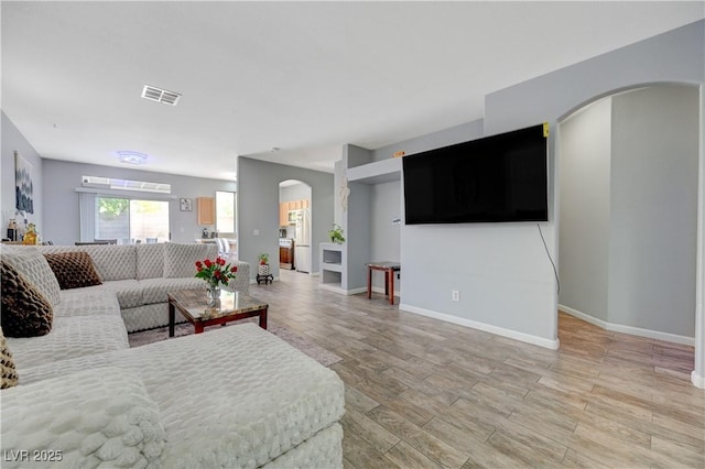 living room featuring arched walkways, light wood-type flooring, visible vents, and baseboards