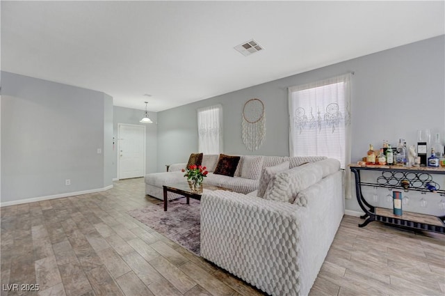 living room featuring light wood-style floors, a healthy amount of sunlight, visible vents, and baseboards