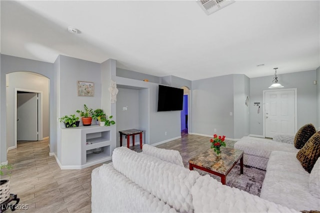 living area with light wood-style floors, arched walkways, visible vents, and baseboards