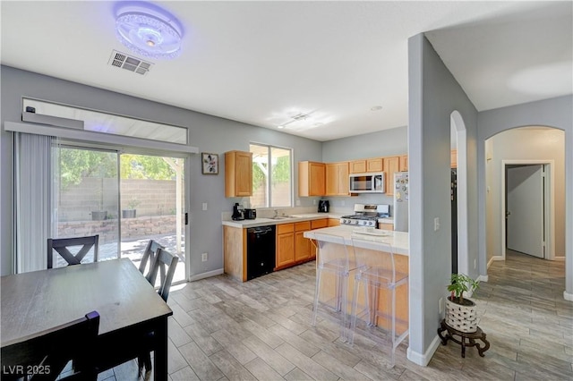 kitchen featuring light wood finished floors, visible vents, arched walkways, stainless steel appliances, and light countertops