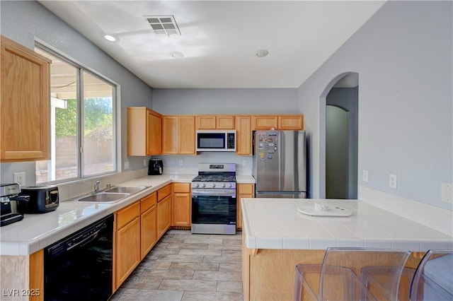 kitchen featuring tile countertops, stainless steel appliances, visible vents, a sink, and a peninsula