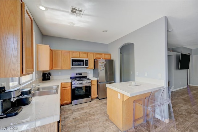 kitchen featuring arched walkways, stainless steel appliances, visible vents, a sink, and a kitchen breakfast bar