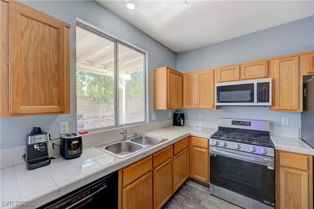 kitchen with tile countertops, appliances with stainless steel finishes, light wood-type flooring, and a sink