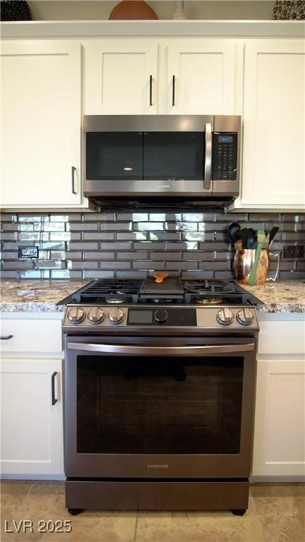 kitchen featuring stainless steel appliances, tasteful backsplash, white cabinets, and light stone countertops