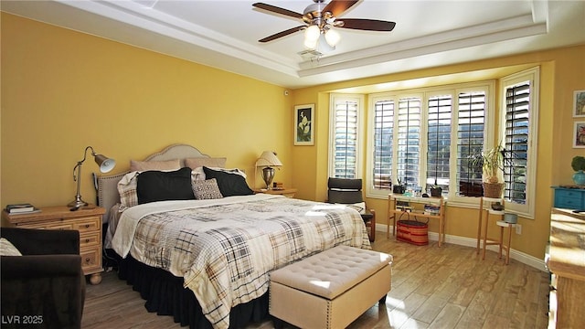 bedroom featuring baseboards, a tray ceiling, ceiling fan, and wood finished floors