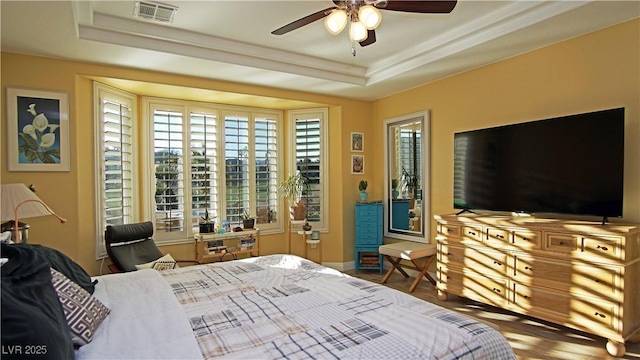 bedroom featuring a raised ceiling, visible vents, a ceiling fan, wood finished floors, and baseboards