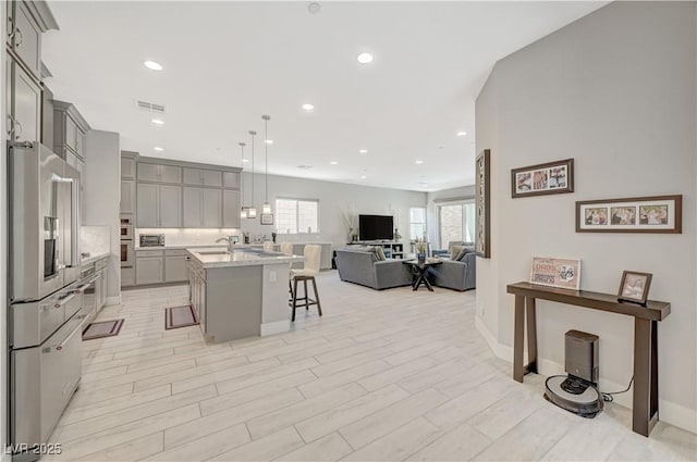 kitchen featuring gray cabinetry, visible vents, open floor plan, appliances with stainless steel finishes, and a kitchen bar