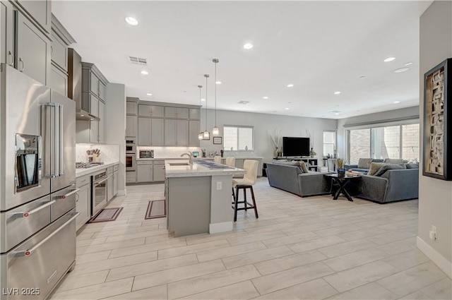 kitchen with visible vents, gray cabinetry, appliances with stainless steel finishes, open floor plan, and wall chimney range hood