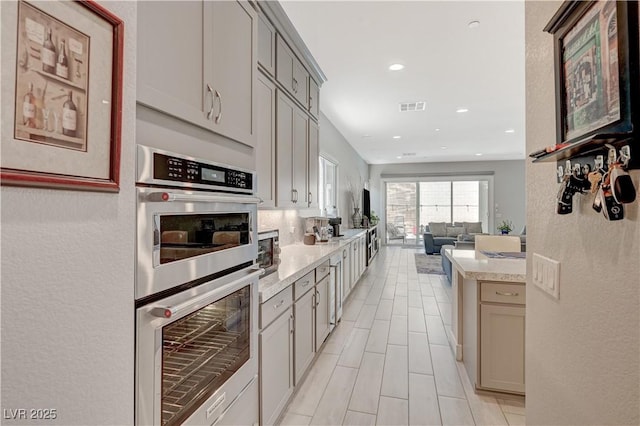 kitchen featuring stainless steel double oven, visible vents, open floor plan, light countertops, and gray cabinets