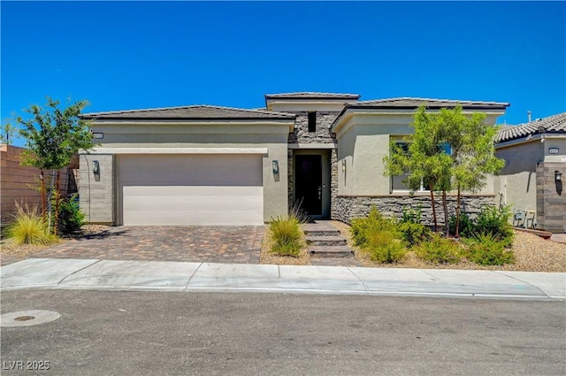 prairie-style house featuring a garage, stone siding, fence, decorative driveway, and stucco siding