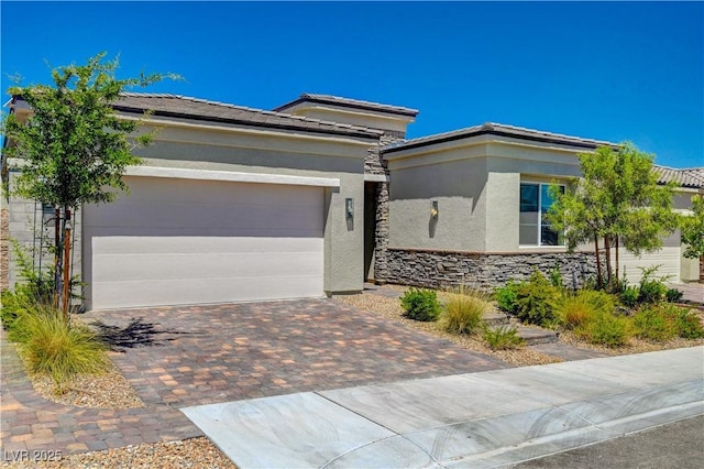 prairie-style house with decorative driveway, stucco siding, an attached garage, stone siding, and a tiled roof