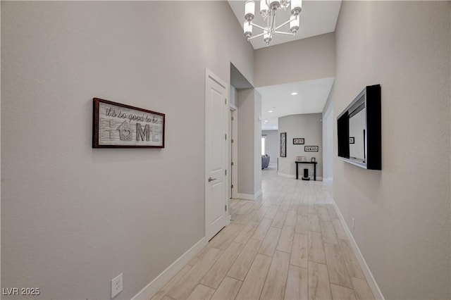 hallway featuring a towering ceiling, light wood-style floors, baseboards, and a chandelier