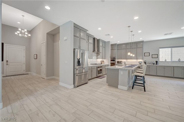 kitchen with wall chimney range hood, a kitchen breakfast bar, stainless steel appliances, and gray cabinetry