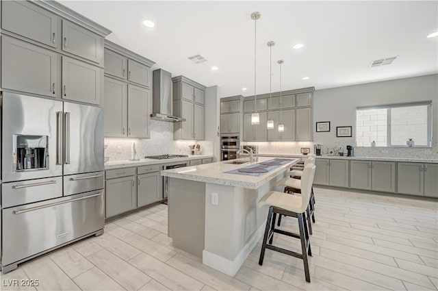 kitchen with stainless steel appliances, visible vents, gray cabinets, decorative backsplash, and wall chimney exhaust hood