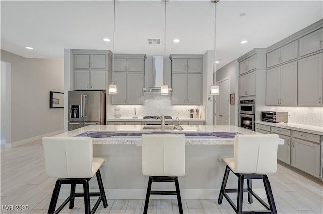 kitchen featuring stainless steel appliances, visible vents, decorative backsplash, gray cabinetry, and wall chimney range hood