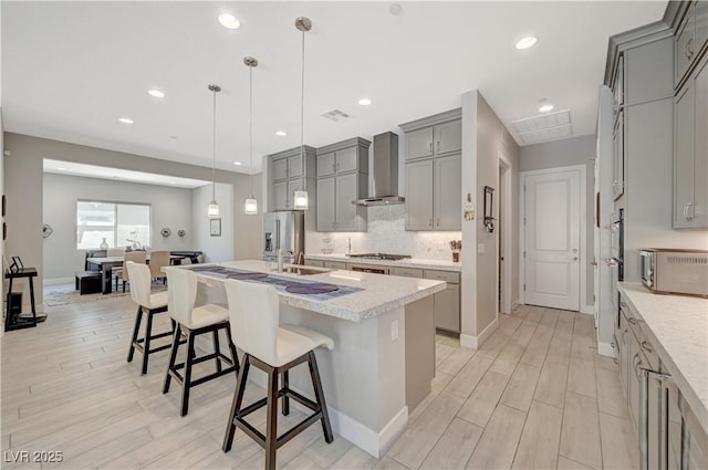 kitchen featuring a breakfast bar area, gray cabinets, decorative backsplash, appliances with stainless steel finishes, and wall chimney exhaust hood