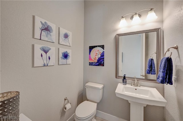 half bathroom with a sink, toilet, and baseboards