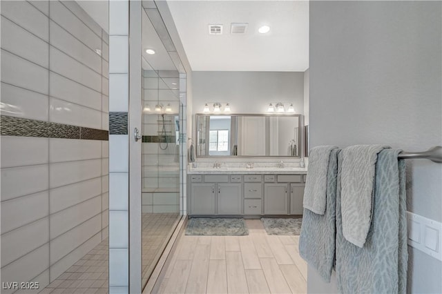 full bath featuring a sink, double vanity, walk in shower, and visible vents