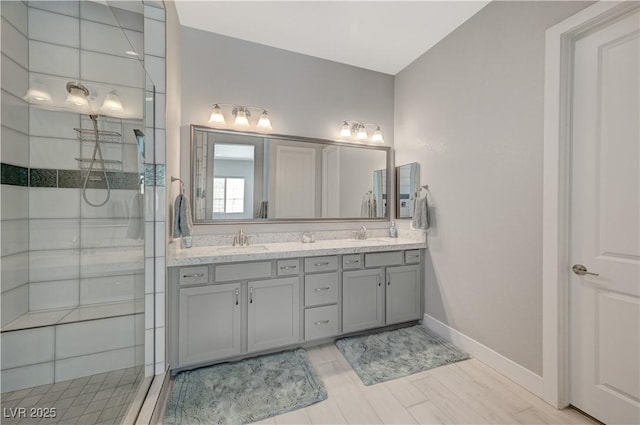 full bath featuring double vanity, baseboards, a tile shower, and a sink