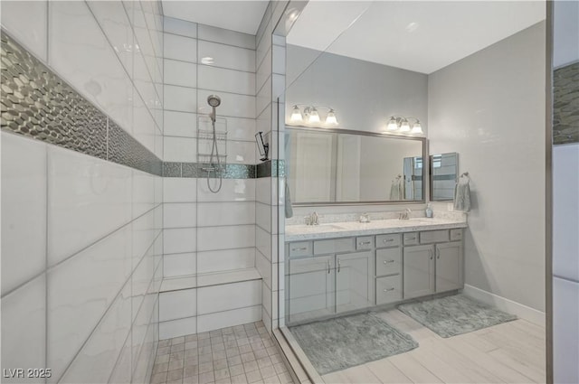 bathroom featuring baseboards, a tile shower, a sink, and double vanity