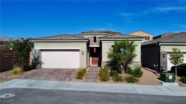 prairie-style house featuring an attached garage, fence, stone siding, driveway, and stucco siding